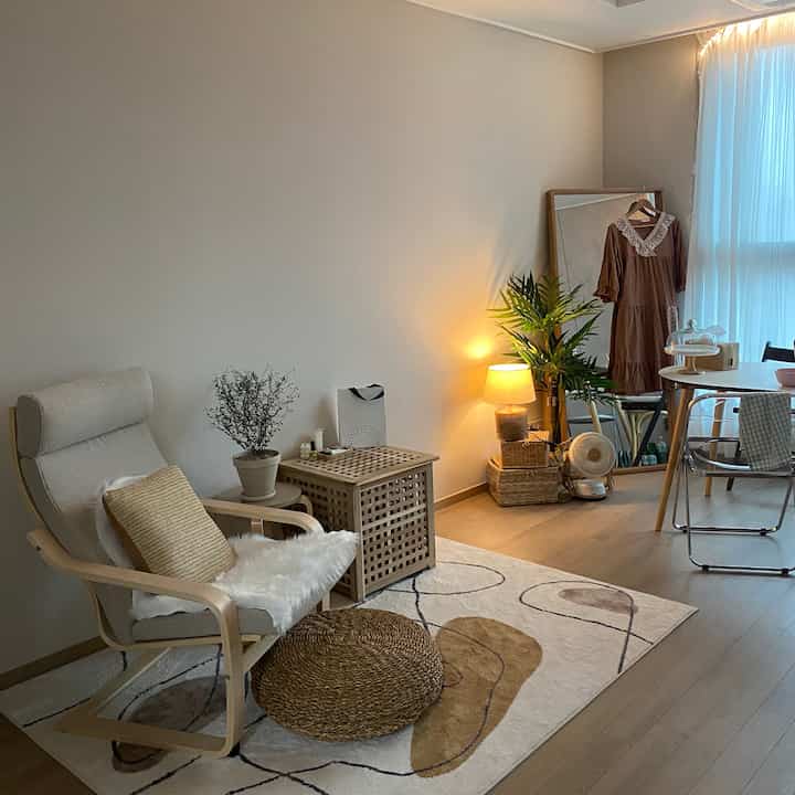 白い壁と木目調家具の一人暮らし用リビング、快適なアームチェアとラグ、温かみのある照明が配置された雰囲気のある空間