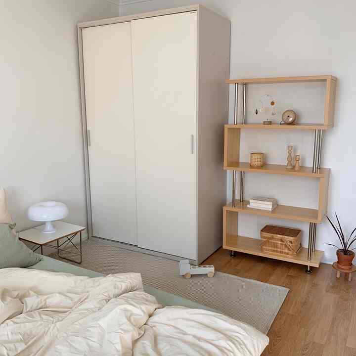 Bright white walls and wood tone furniture create a cozy bedroom featuring beige duvet cover and minimal shelves in a natural modern style