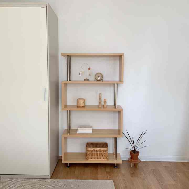 ナチュラルな色調のリビング、白い壁の前に木製と金属の4段シェルフと鉢植えが整然と配置された印象的な空間