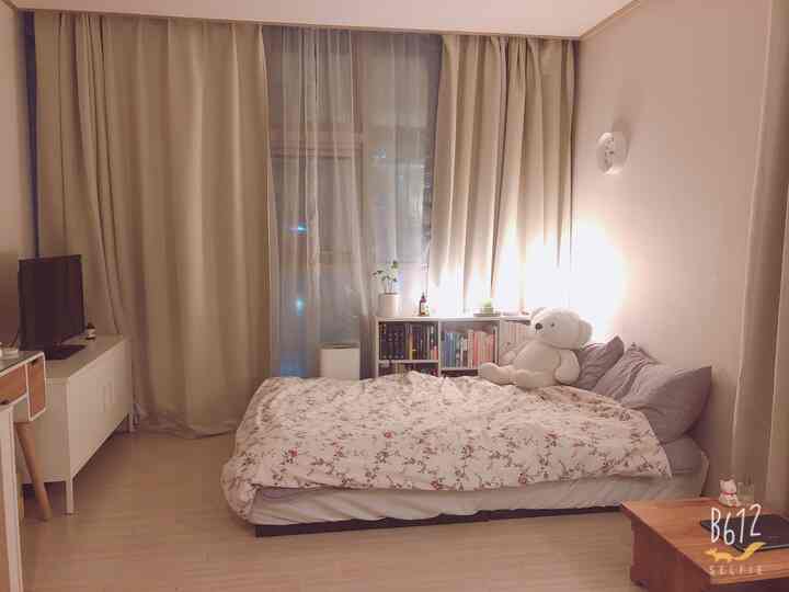 ベージュとホワイトの色調の寝室、ベッド横に本棚がナイトテーブルの役割を果たし、温かみのある雰囲気のあるインテリア