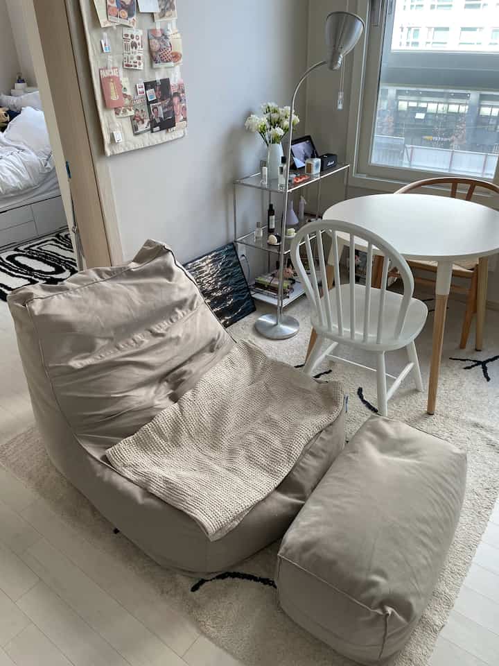 ベージュとホワイトのナチュラルなダイニング、ビーズクッションソファ、木製椅子、ラグ、フロアランプが配置された雰囲気のある空間