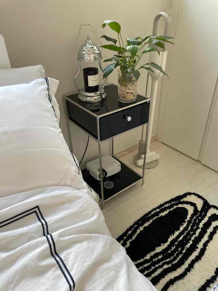 Modern bedroom in white and black tones featuring a nightstand with candle and plant, creating a clean atmosphere