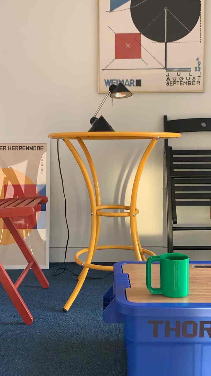 A compact space featuring a yellow round table with colorful accessories, posters on the wall and a blue rug, showcasing a cozy interior