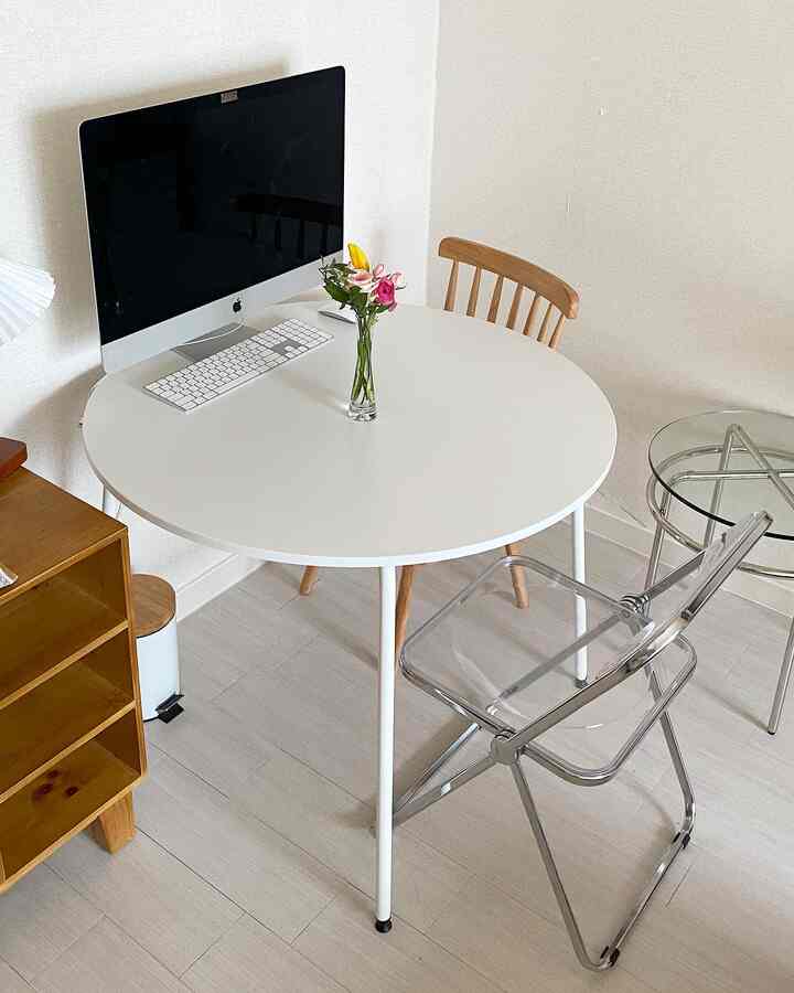 White-toned space featuring a round table with a computer and vase, creating a clean home office area
