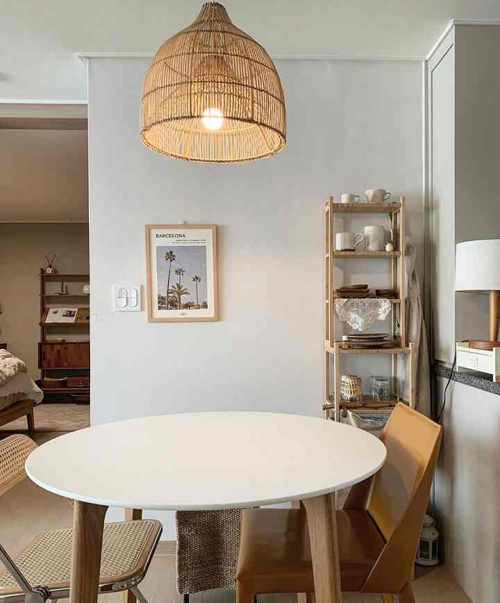 ナチュラルなブラウンとホワイトの色調のダイニング、円形ダイニングテーブルとラタンのペンダントライト、多様な椅子が配置された雰囲気のある空間