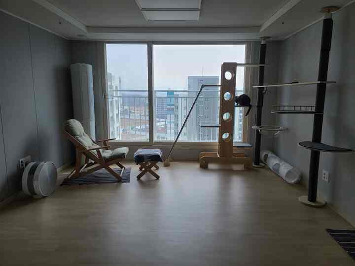 A natural-toned living room with white walls, wooden floor and furniture, featuring a cat tower and reclining chair in a minimalist setup