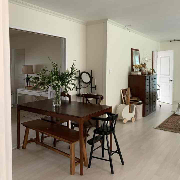 White and brown toned dining room featuring wooden dining table and bench with a glass vase of flowers, creating a cozy space