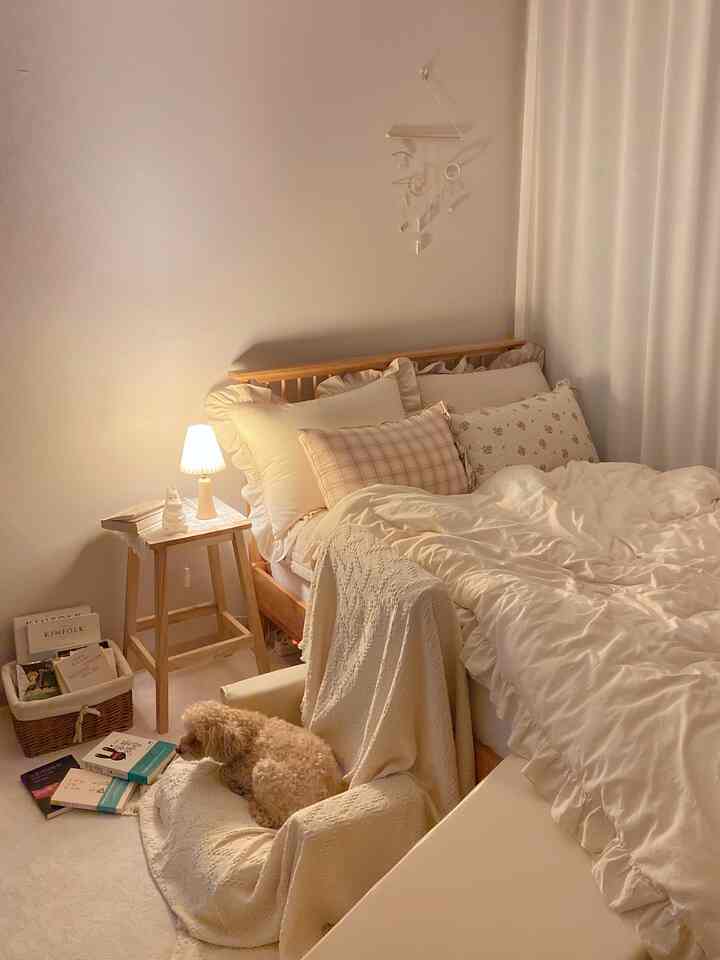 暖かみのあるベージュとアイボリー調の寝室、木製ベッドとフリル寝具、小さな犬が座る居心地の良い空間