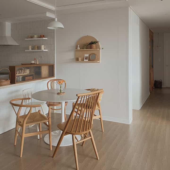 Natural dining room in white and wood tones, featuring a round table with rattan and wooden chairs in a simple setting