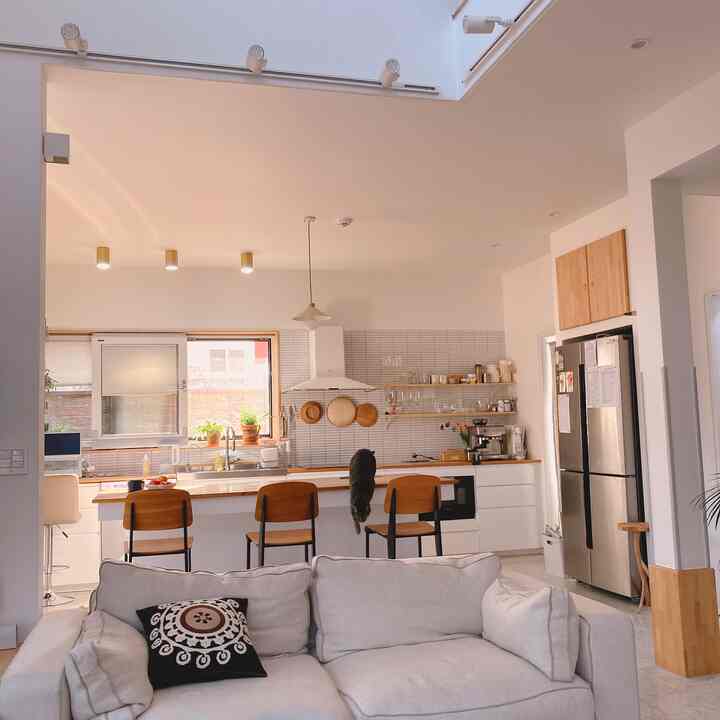 A white and wood-tone living and kitchen space featuring three wooden dining chairs and a cat in a cozy natural interior