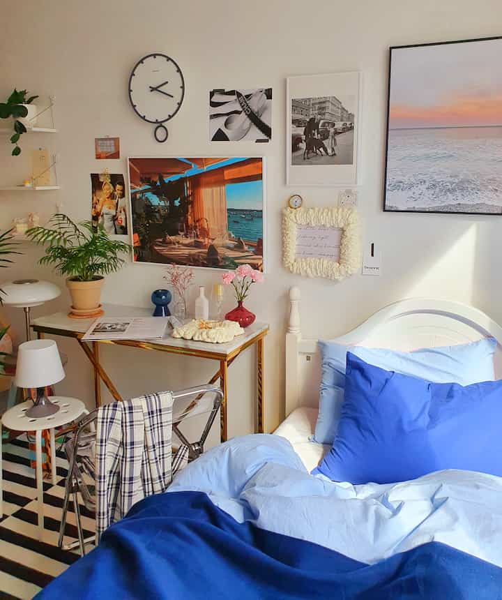 ホワイトとゴールドトーンの寝室、ブルーの寝具とコンソールテーブル、植物が配置された雰囲気のある空間