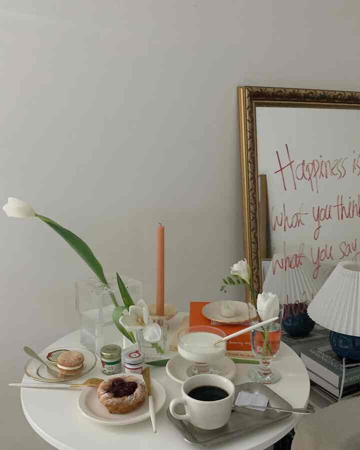 白を基調としたリビングのテーブルに、コーヒーやデザート、花瓶、ゴールドの縁取り食器が配置された雰囲気のあるおうちカフェ空間