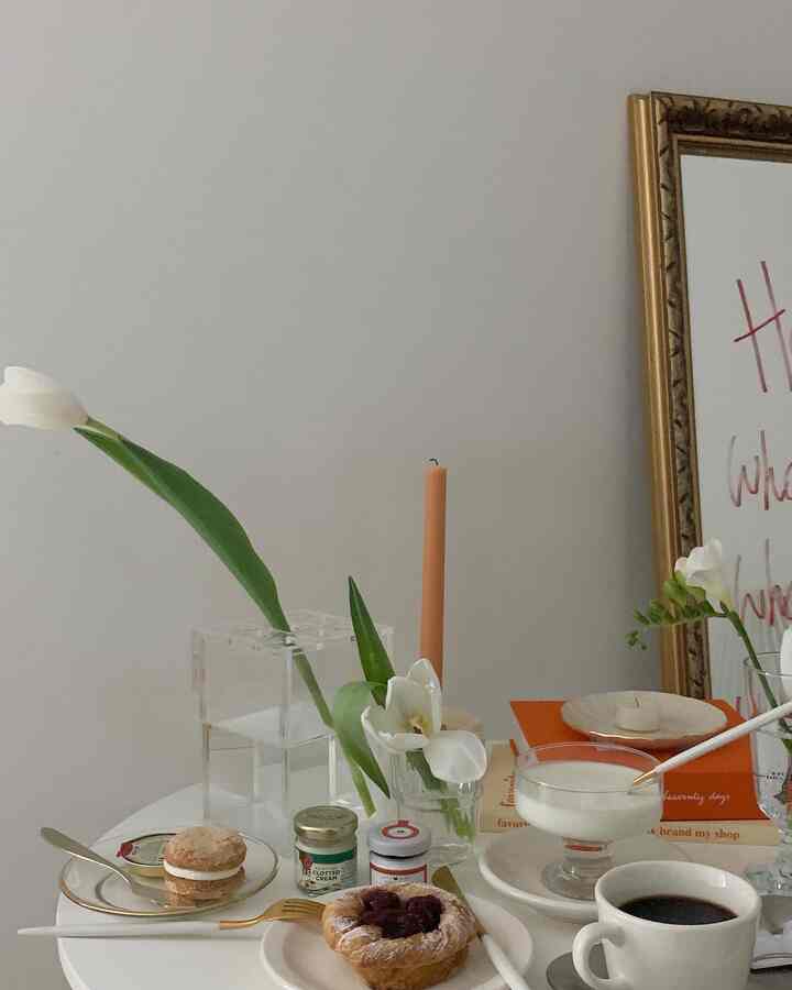 白とゴールドの色調のリビングのダイニングテーブル、ブランチ用食器と花、キャンドルが配置された雰囲気あるインテリア