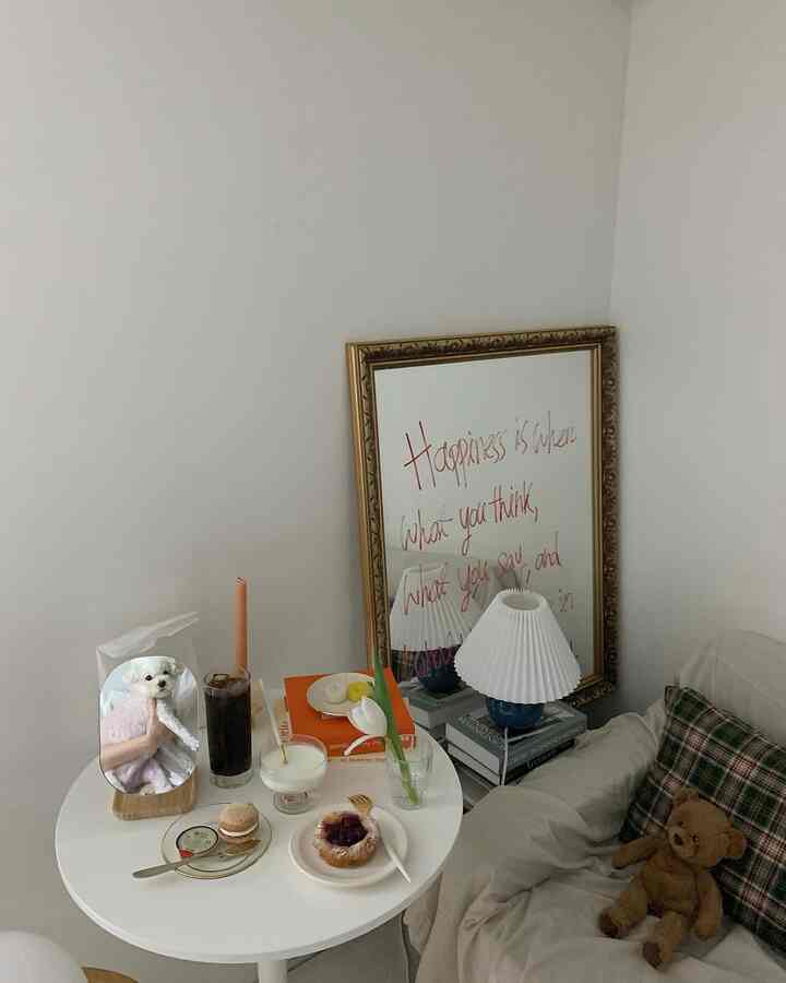 ホワイトとベージュの色調のダイニング、丸いダイニングテーブルにコーヒーとデザートが置かれ、大きな金色の額縁の鏡とテーブルランプが配された雰囲気のあるインテリア