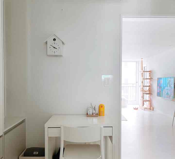 Bright white-toned bedroom corner with a desk and chair, adjacent living room features a wooden cat tower