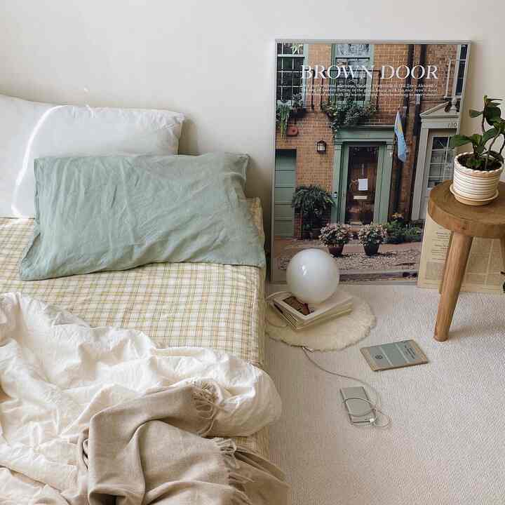 自然なグリーンとベージュのトーンの寝室、ベッドとポスター、木製スツールと植物が配置された雰囲気のあるインテリア