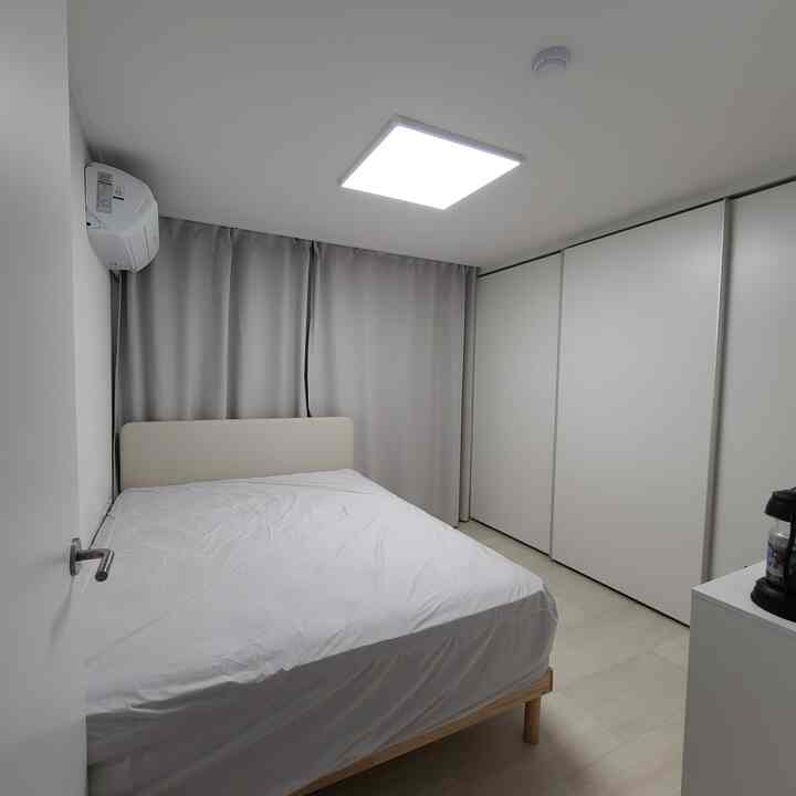 A simple bedroom in white and beige tones featuring a centrally placed bed and a large built-in closet on the right