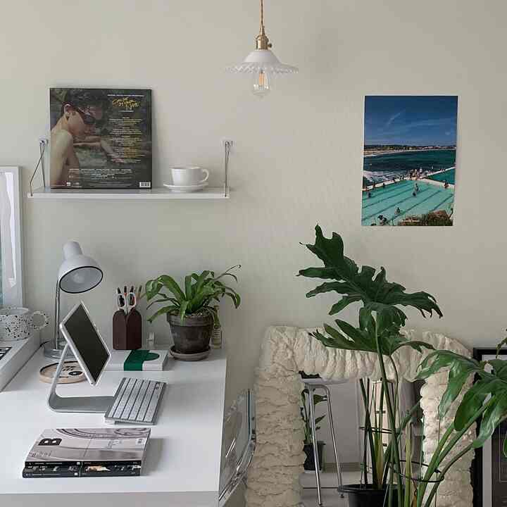 A white and green study space featuring a desk and a shelf with a teacup, creating a simple and cozy atmosphere