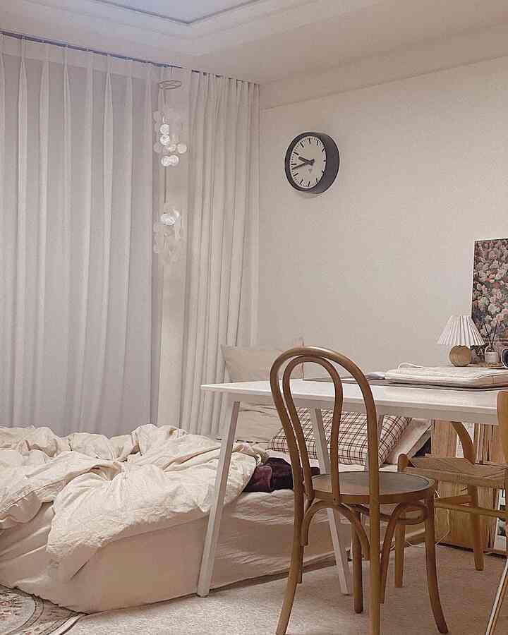 白とベージュのトーンの小さな寝室、床ベッドとダイニングテーブルが配置された落ち着いた雰囲気のインテリア