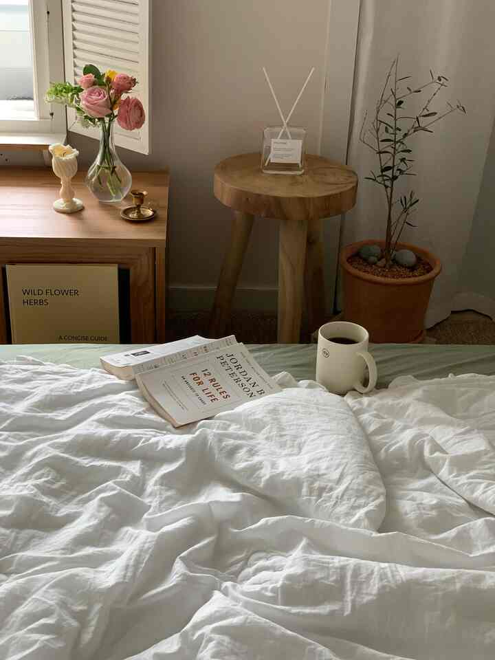 Cozy bedroom with white bedding, wood tone furniture, plants, and a diffuser arranged naturally