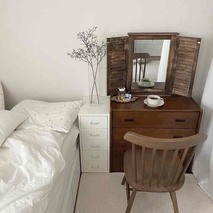 白い壁とベッドがある寝室、木製ドレッサーと木製椅子が配置されたナチュラルな空間