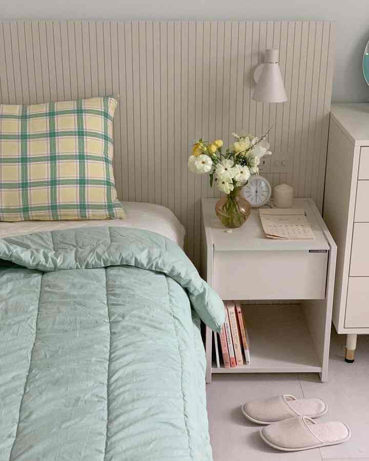 Cozy bedroom with white wall panels and mint duvet cover, featuring a nightstand with vase and clock