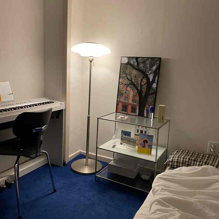 柔らかな照明と青いラグが敷かれたワンルーム、ピアノと棚が配置されたモダンな雰囲気の寝室空間