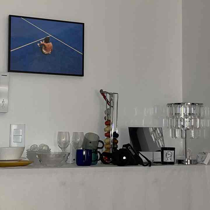 白を基調とした玄関、壁に青い絵画の額縁が掛かり、棚にはカップと照明が整然と配置された雰囲気のあるインテリア