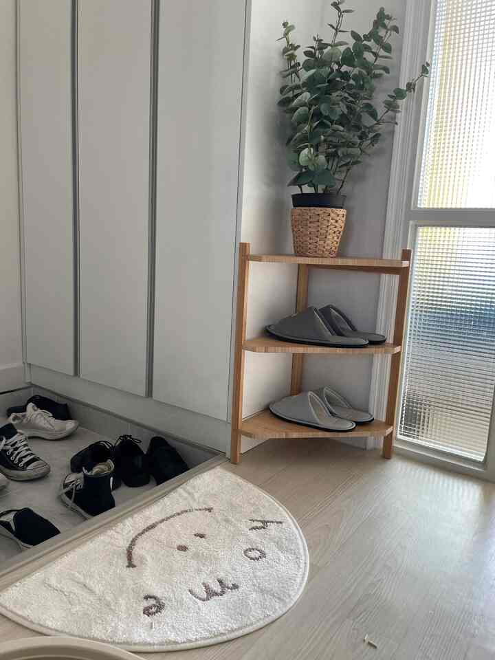 白と木目調の玄関、コーナーシェルフに複数のスリッパが整然と並べられた雰囲気のある空間