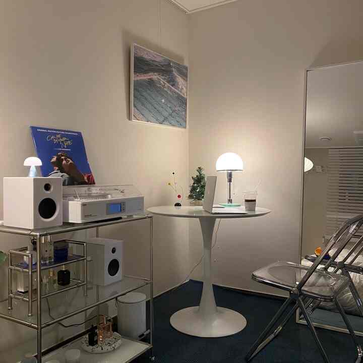 ホワイトとブルーを基調としたワンルーム、丸テーブルとクロームシェルフが配置されたミニマルで整ったワークスペース