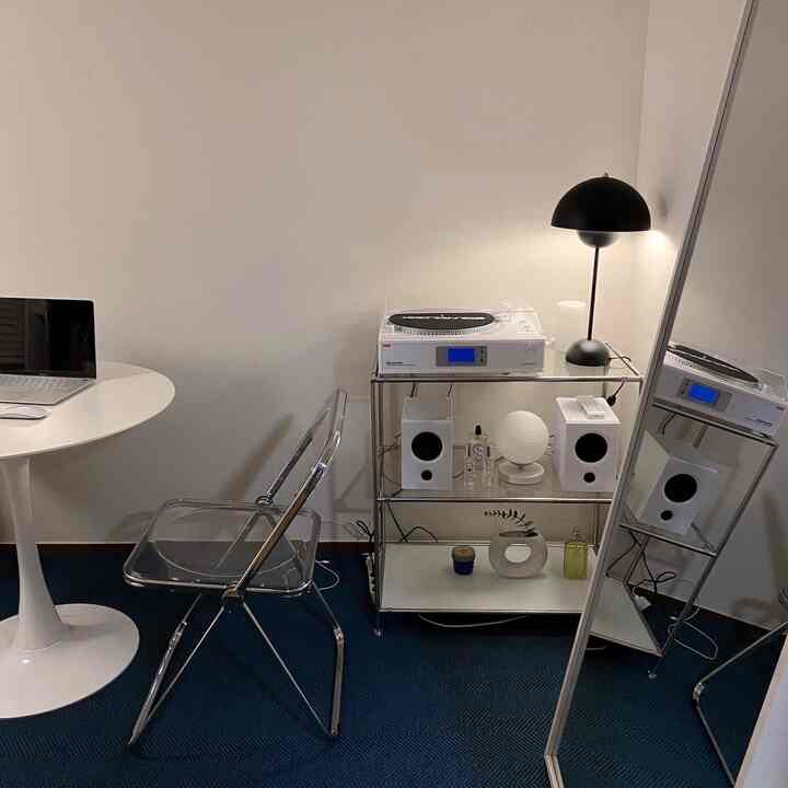 White-toned walls and furniture with blue carpet in a compact single household space, featuring a transparent chair and full-length mirror in a simple atmosphere