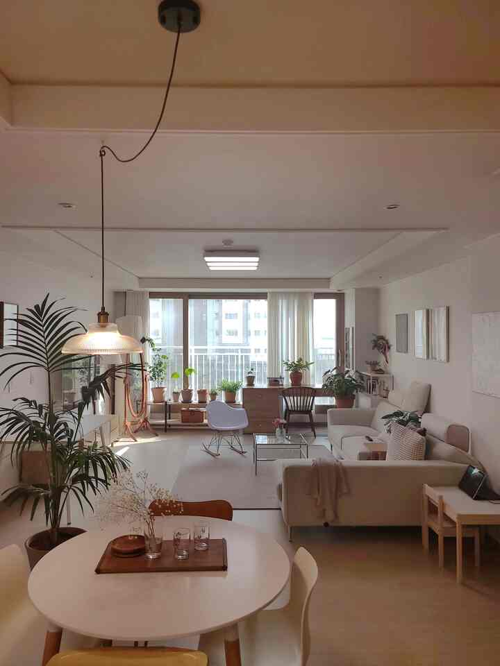 Beige and white toned living room featuring round dining table, fabric sofa, and various plants by window in cozy natural modern style