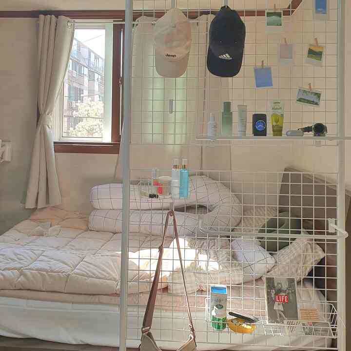 ベージュと白を基調とした狭いワンルーム寝室、メタルグリッドの間仕切りとシンプルな寝具が配置された雰囲気のあるインテリア