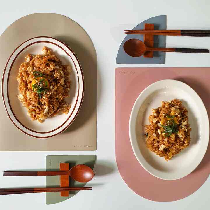 Modern table setting with oval plates and wooden cutlery rests on beige, pink, and olive placemats