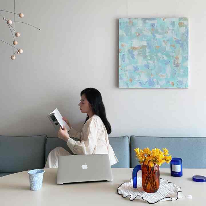 Bright white walled living room with blue sofa, dining table featuring yellow flowers creating a cozy, minimalistic home office atmosphere
