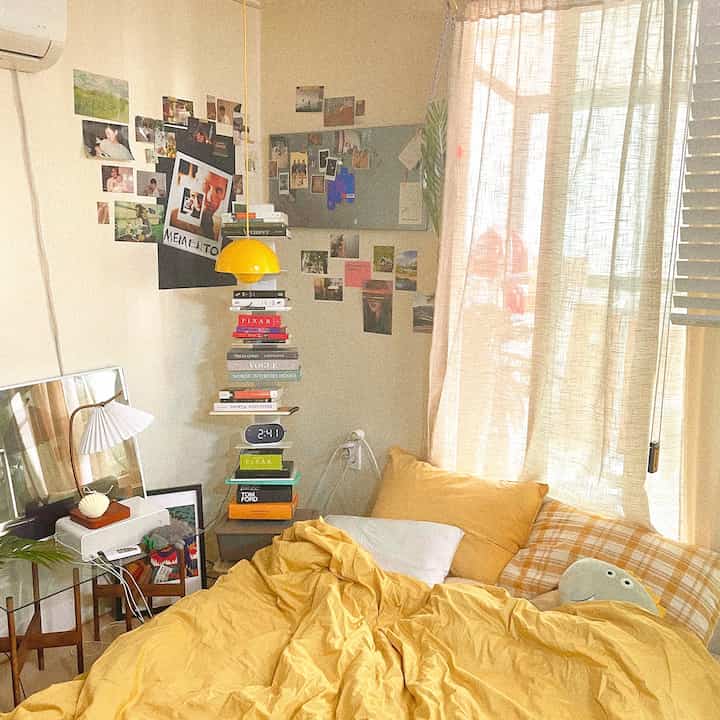 明るい黄色のトーンの寝室、黄色いペンダントライトと寝具が配置された居心地の良いワンルームインテリア