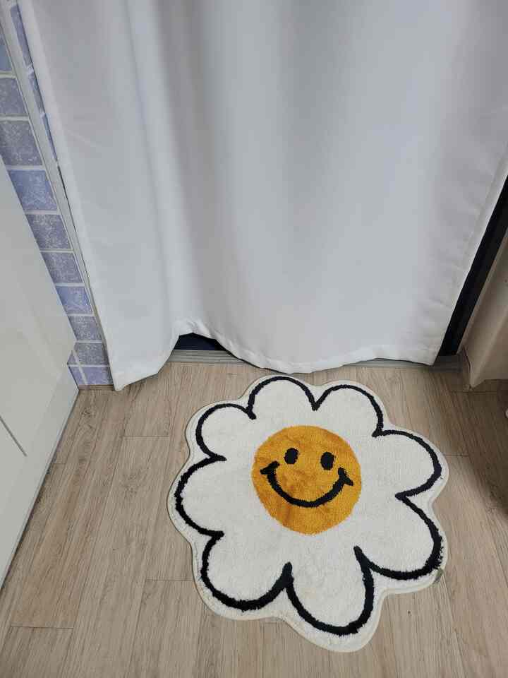 白と黄色の花形スマイリーフェイスのバスマットが配置された玄関前の床