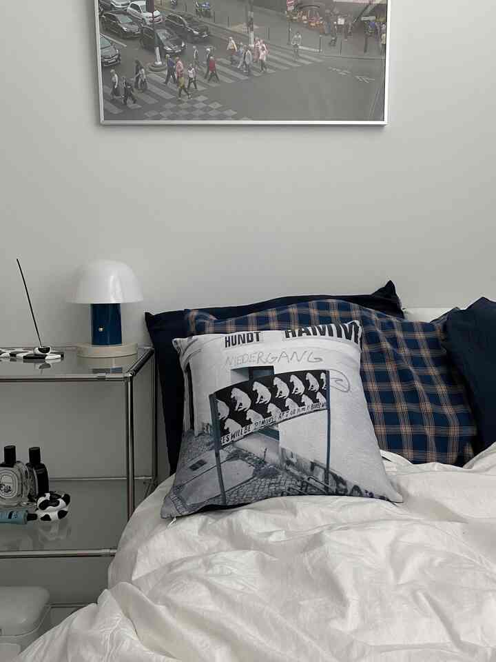 白とネイビーの色調の寝室、白いベッドにネイビーの枕、壁にアートポスターとサイドテーブルのあるシンプルなインテリア