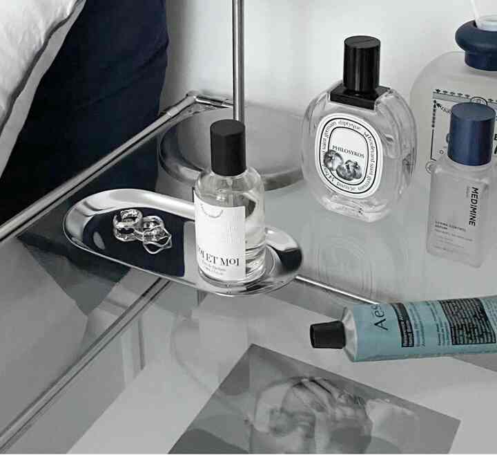 銀色のトレイと香水瓶が置かれた清潔感のある白い寝室のナイトテーブル、ミニマルな雰囲気