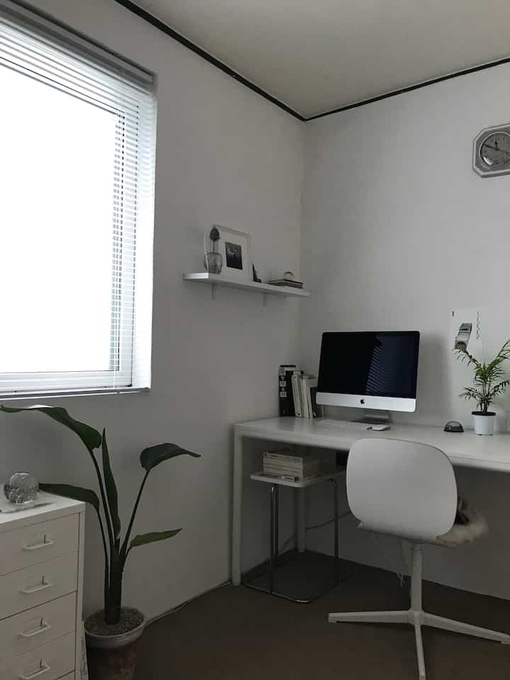 White-toned home office space featuring a simple shelf, desk, and office chair in a minimalistic work environment