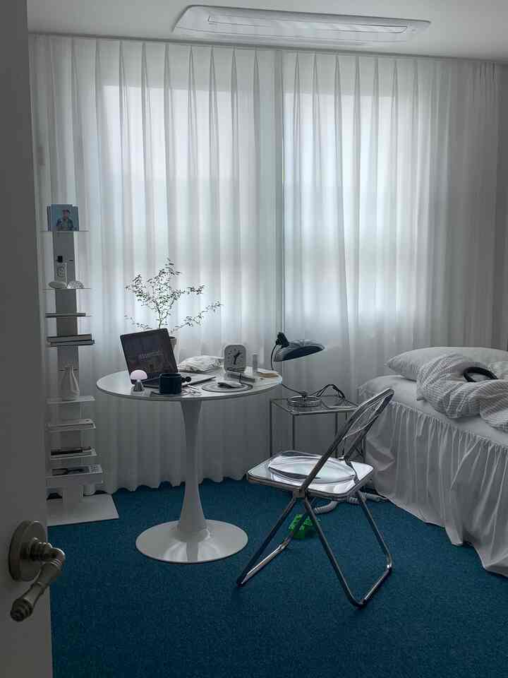 白と青のトーンのワンルーム寝室、ミニマルな家具とナイトテーブル、掛け布団カバーが配置された清潔感のある空間