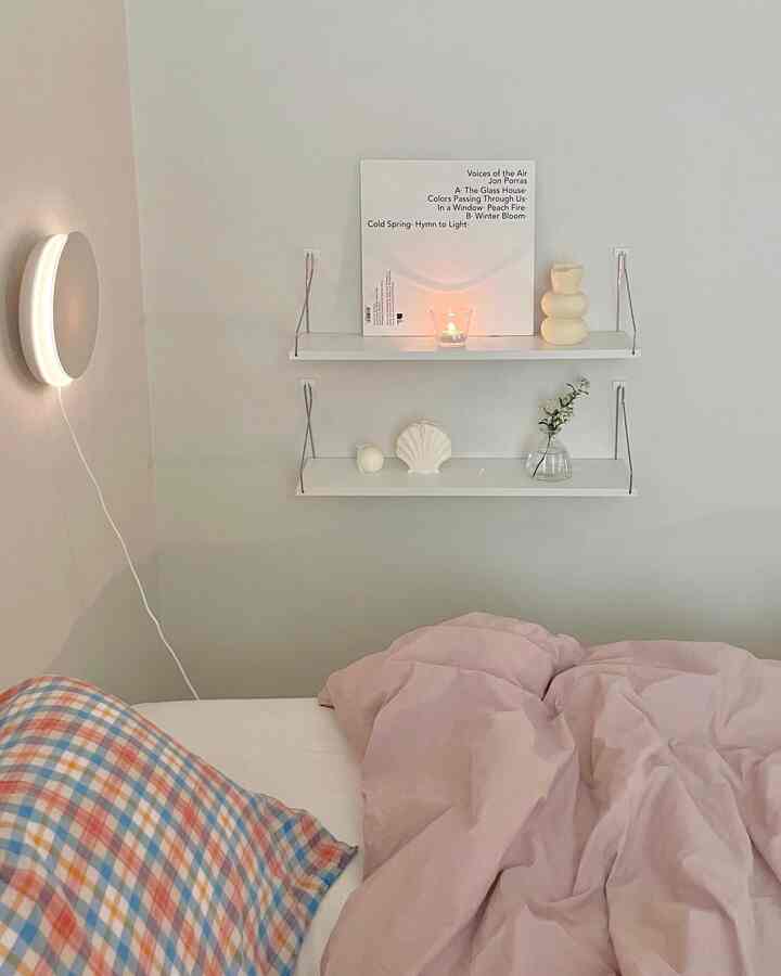 Cozy bedroom space with white walls and shelves, featuring pink bedding