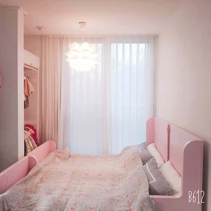Kids' room with pink bed and white sheer curtains, soft and bright atmosphere