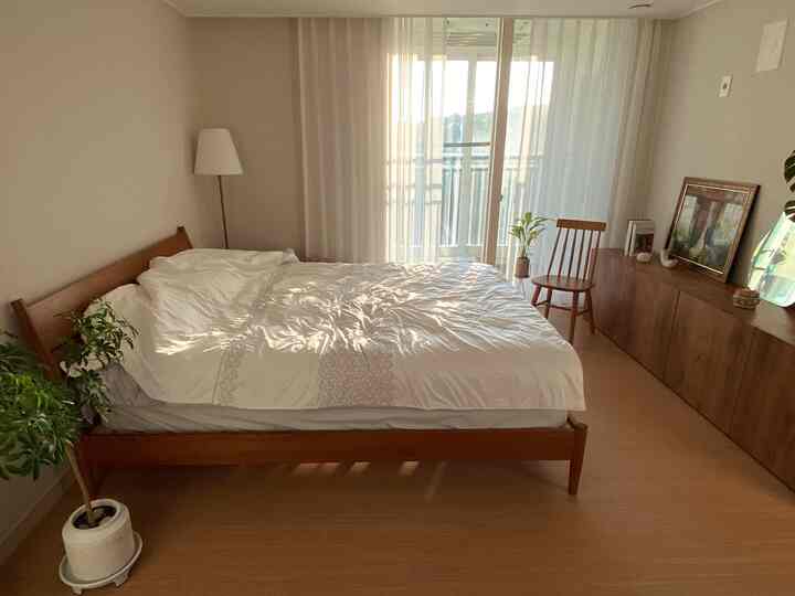 白いカーテンと木目調の家具が配置された暖かく自然な雰囲気の寝室