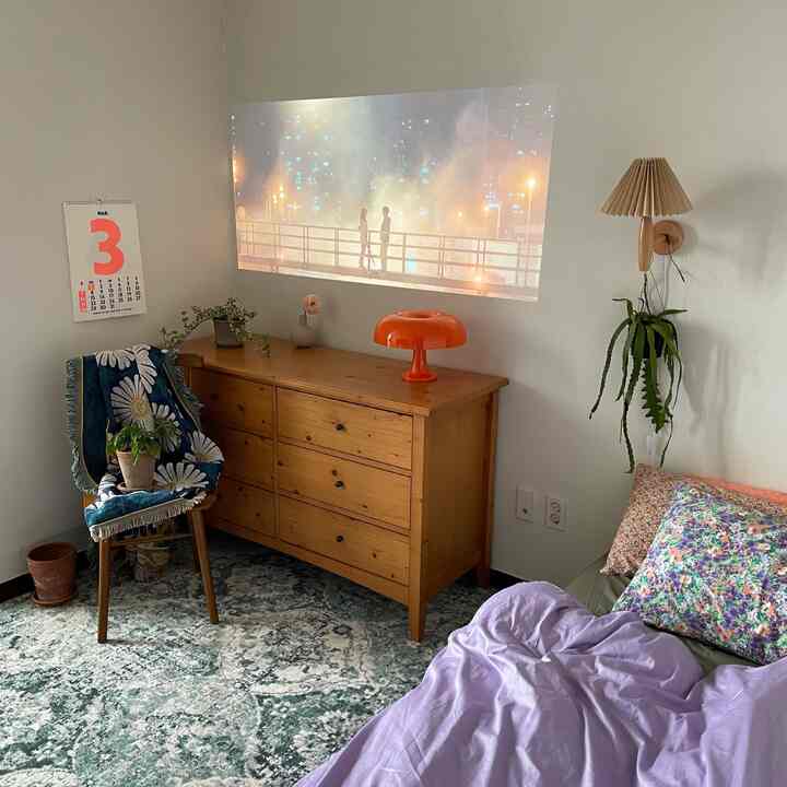 ナチュラルな色調と木製家具が調和した寝室、壁にはビームプロジェクターの映像が映し出される雰囲気のあるインテリア