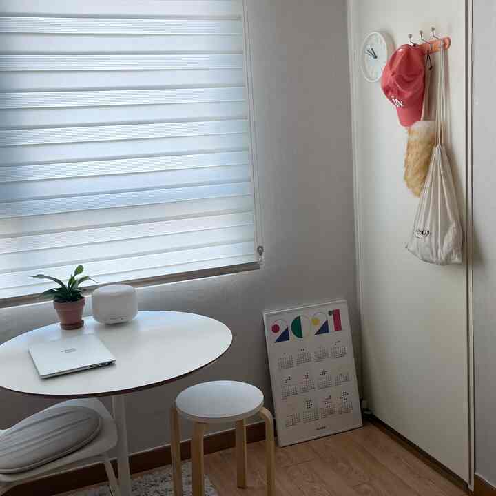 アイボリートーンの小さなワンルーム、丸い白いテーブルとスツールが配置された落ち着いた清潔感のある空間