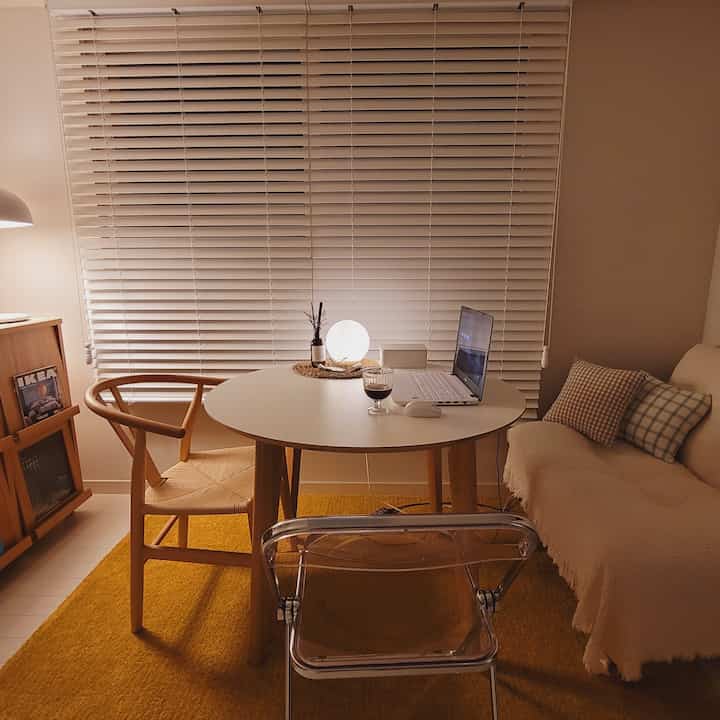 暖かいナチュラルカラーのワンルームのホームオフィス空間、丸テーブルとソファ、クッションが配置された居心地の良いインテリア。