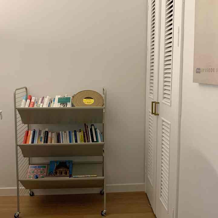 Natural color small room with a mobile bookshelf filled with books and a vintage film reel placed against a neutral wall