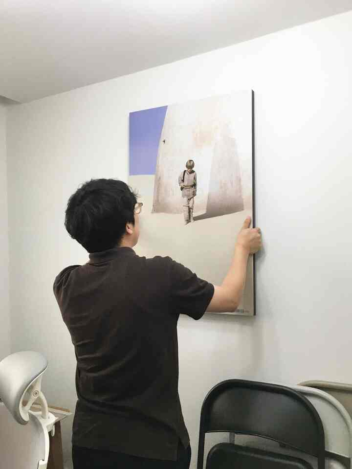 白い壁のホームオフィス空間で、茶色の服を着た人物がポスターを掛けている印象的な空間