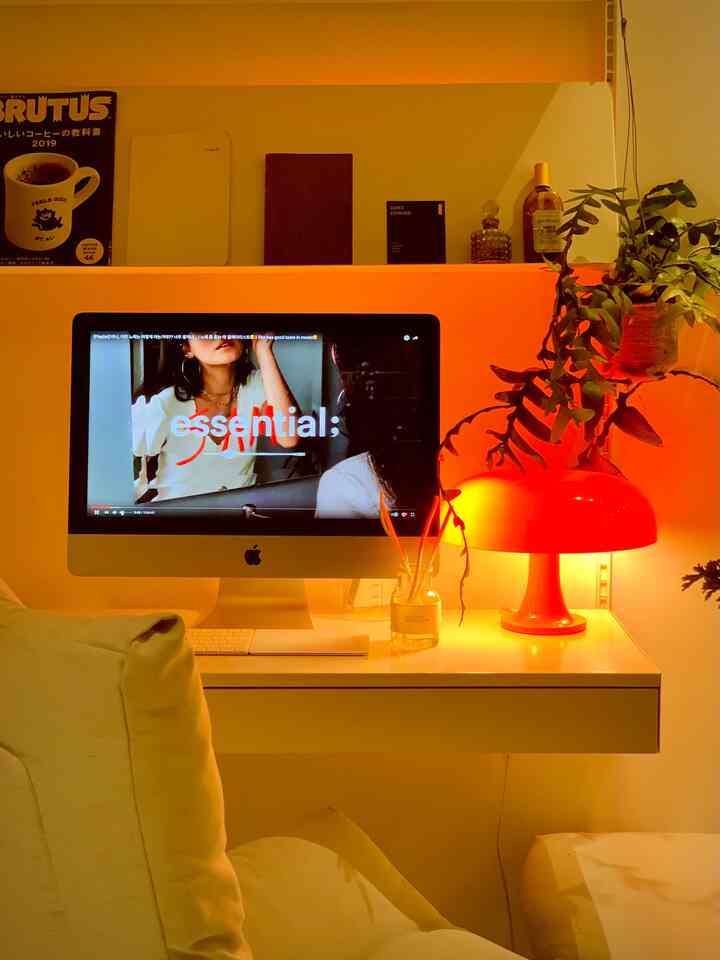 White and orange toned home office featuring a modern computer, orange table lamp, and a plant with a tidy atmosphere
